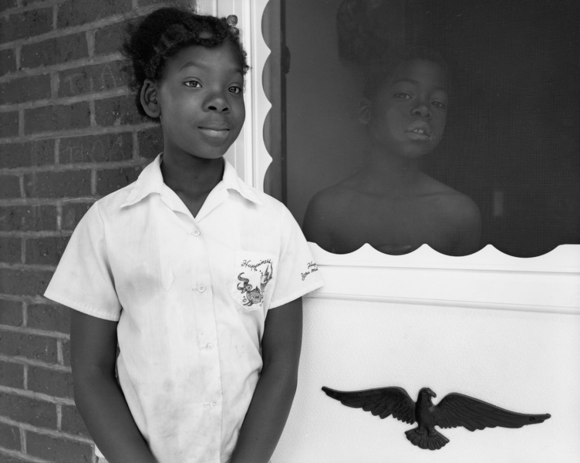 Black-and-white photograph of two children standing on either side of a screen door