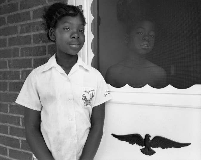 Black-and-white photograph of two children standing on either side of a screen door