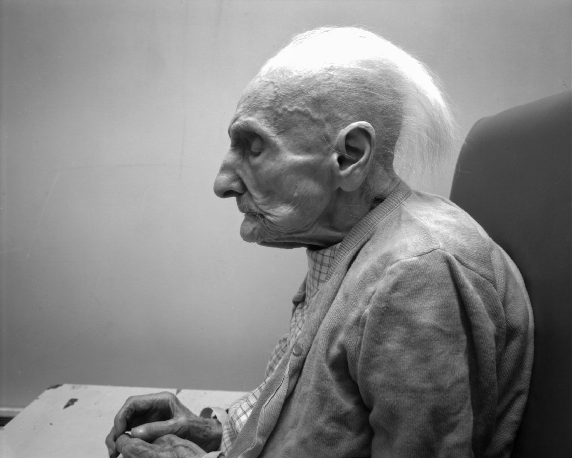 Black-and-white photograph of the profile of a seated elderly woman