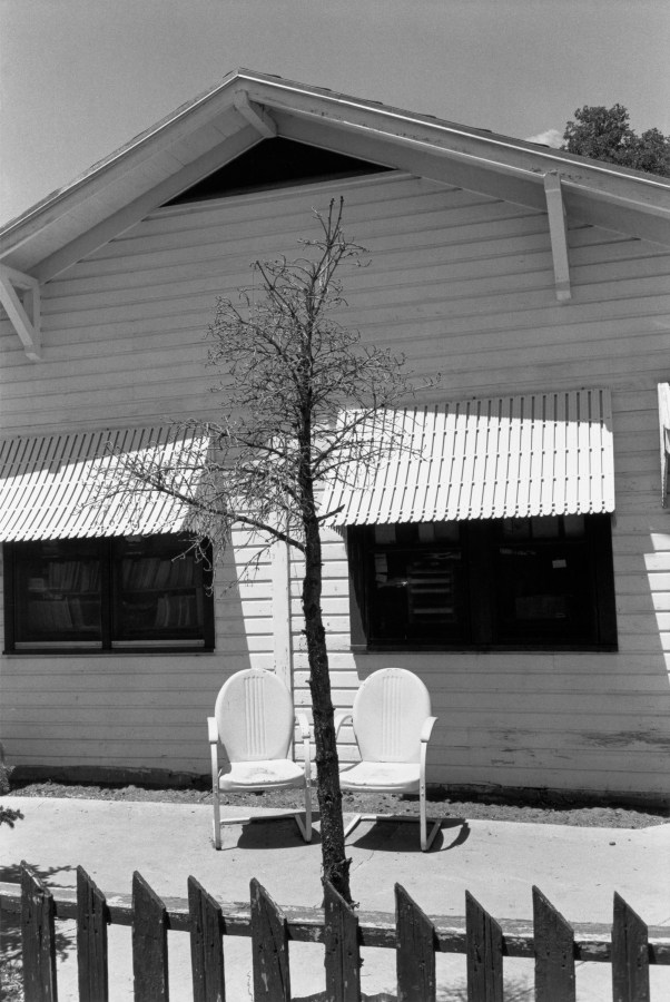 Black and white photograph of house exterior with a tree framed between two chairs