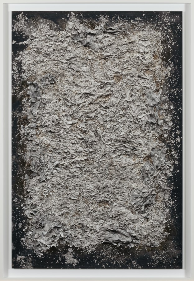 Color image of a color photograph depicting a neat pile of burnt documents on black background framed in white