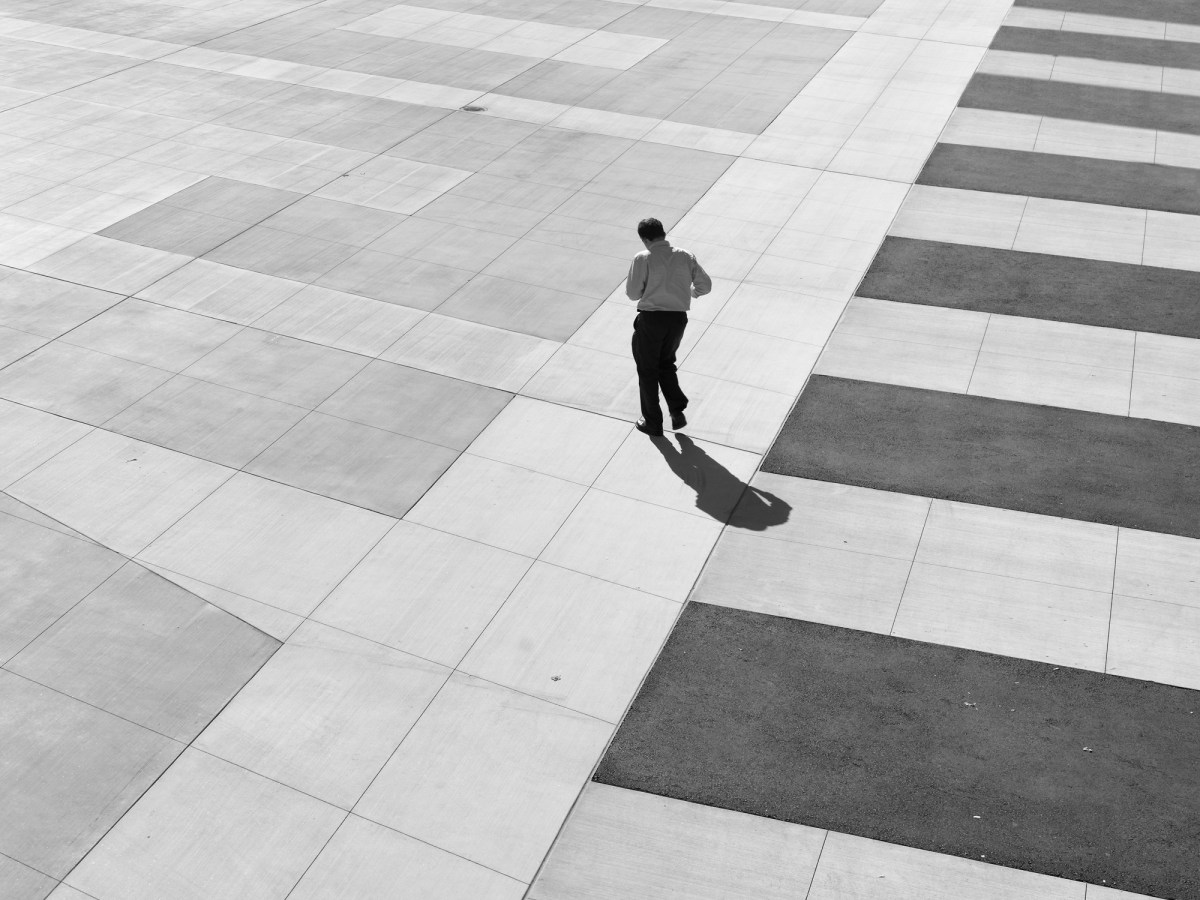 Black and white photograph of a lone man walking across an empty courtyard