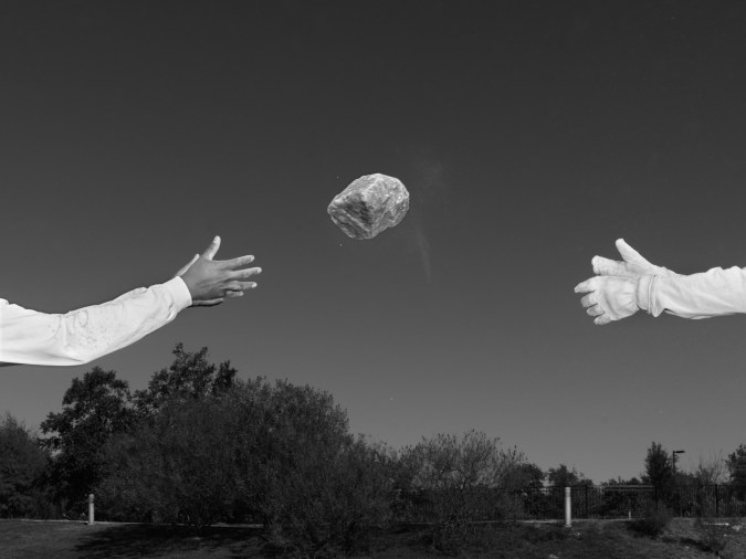 Black and white photograph of two people tossing a rock outdoors