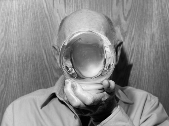 Black and white photograph of man holding glass globe in front of face causing distortion