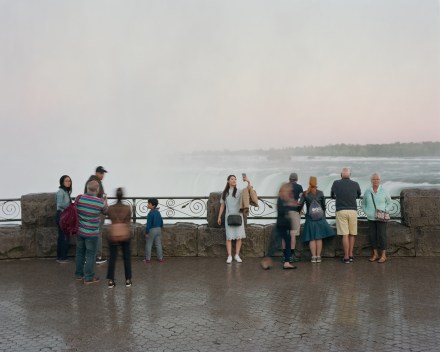 Color photograph of people standing by a fence overlooking a waterfall