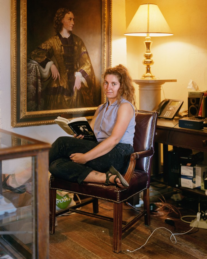 Color image of a seated woman with book in hand looking towards camera