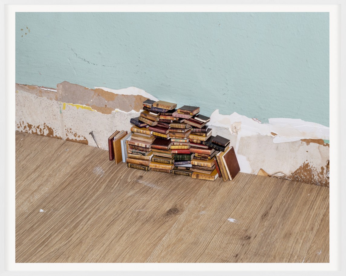 A color photograph shows a pile of miniature leather-bound books stacked against a pale blue wall.