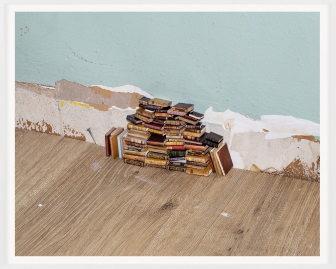 A color photograph shows a pile of miniature leather-bound books stacked against a pale blue wall.