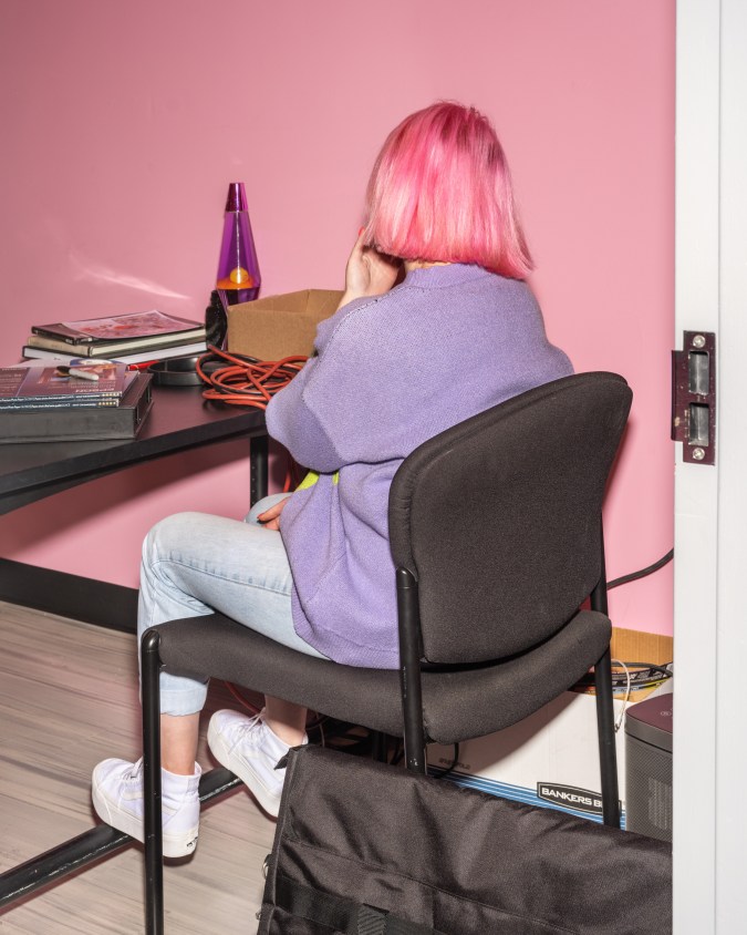person with pink hair wearing a purple sweater sitting at a desk