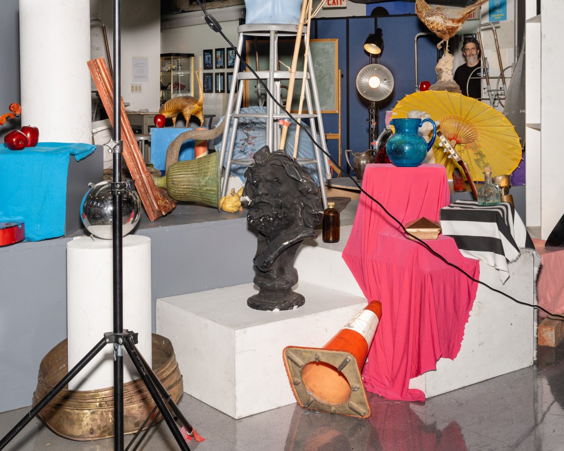 A color photograph shows an array of bright props chaotically arranged on plinths