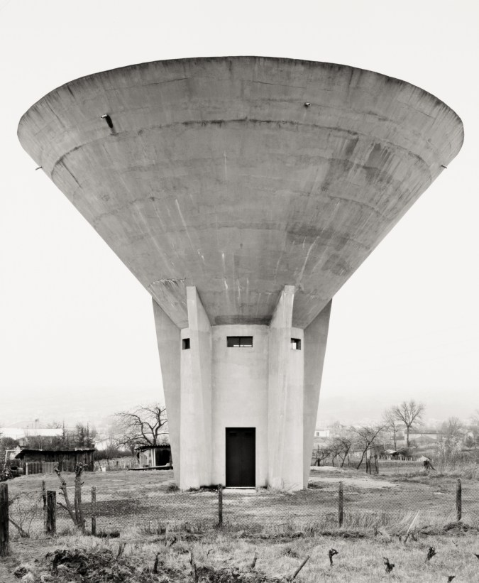 Black and white photograph of a water tower in a grass field