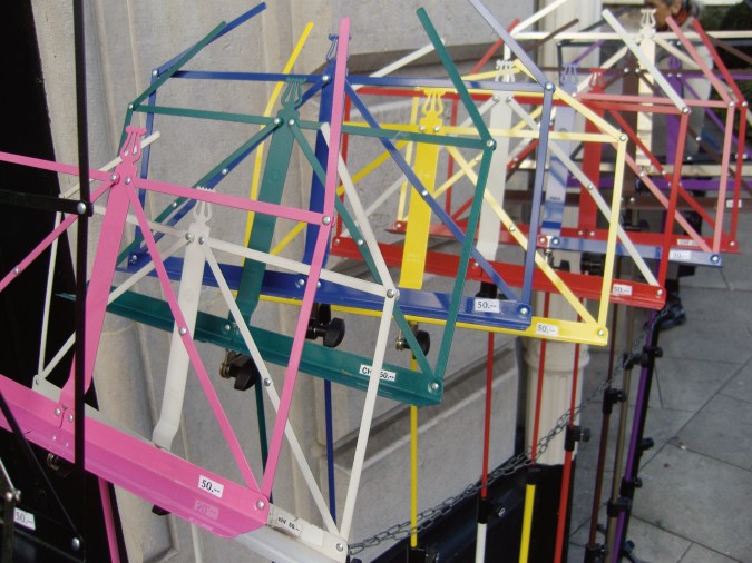 A color photograph of multi-colored music stands, lined up outside