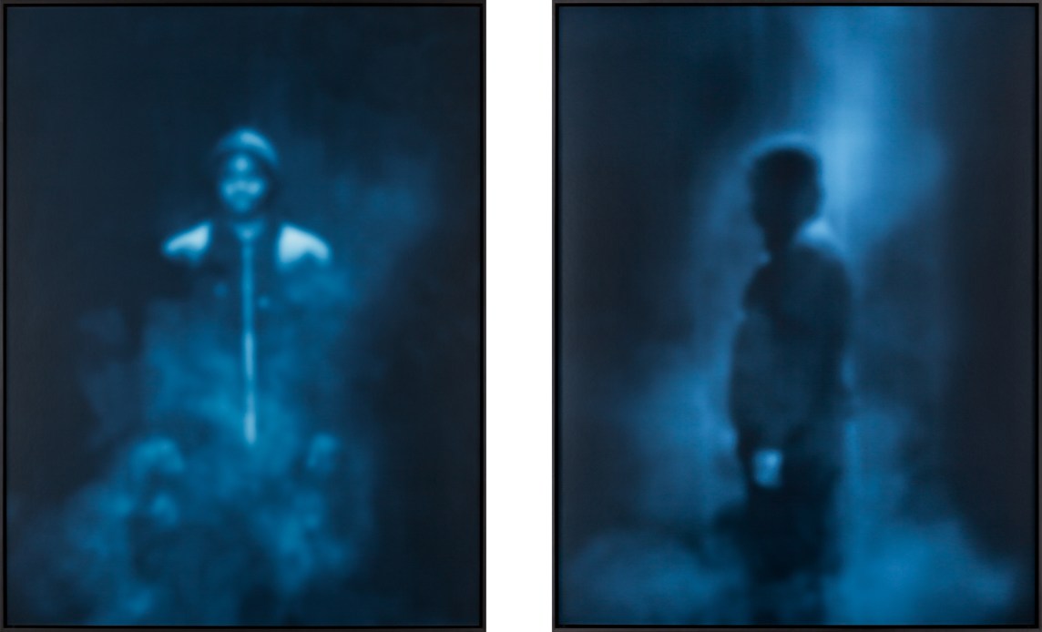 Two framed blue-toned, soft-focus photographs, one depicting a boy in a hat and hooded sweatshirt facing forward, and one in profile.