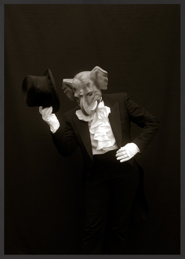 Framed black and white photograph of suited figure with white gloves and top hat wearing a mask depicting an elephant