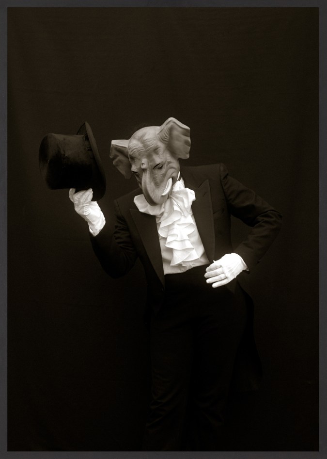 Framed black and white photograph of suited figure with white gloves and top hat wearing a mask depicting an elephant