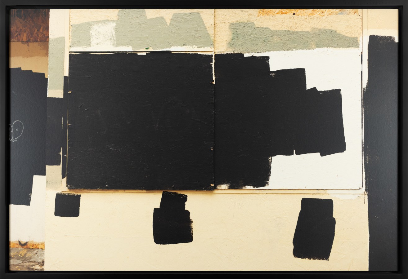 Color image of boarded up store front with paint splotches covering graffiti in black frame