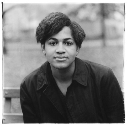 Black and white photograph of a young man seated in a city park