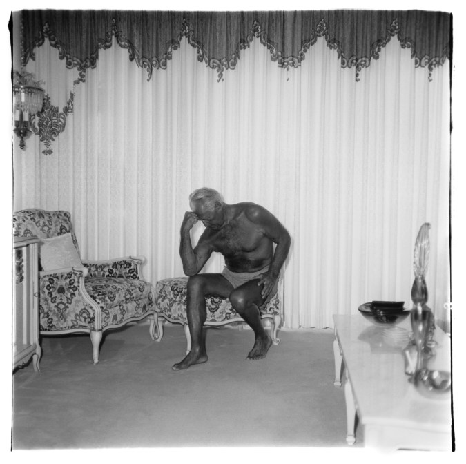 Black-and-white photograph of a tanned man sitting with his head resting on his hand