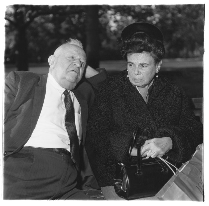 Black-and-white photograph of a man resting his head on his hand and a woman holding a purse and shopping bag