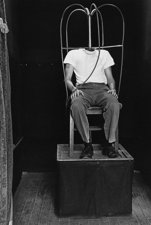 Black-and-white photograph of a headless man sitting on a chair on top of a pedestal
