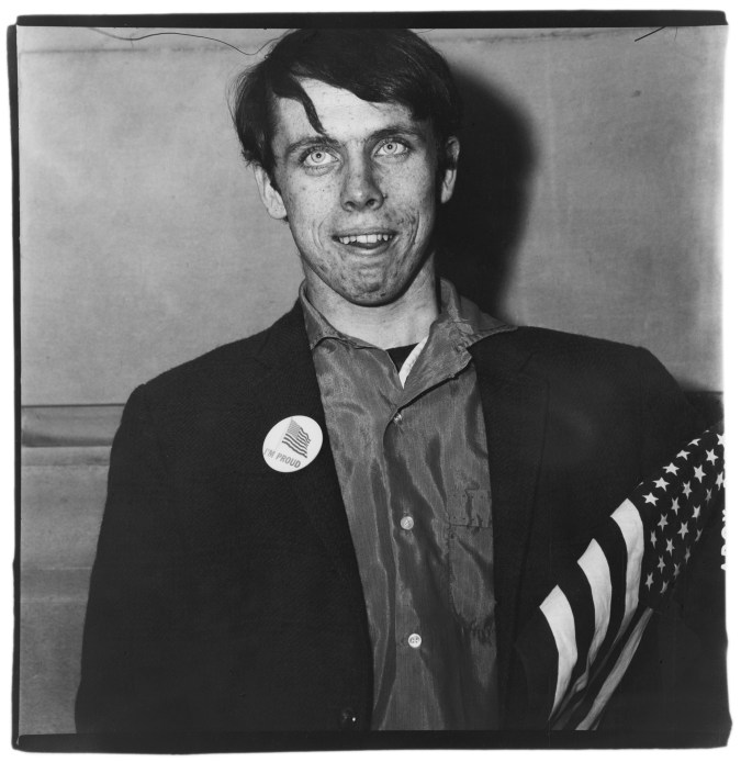 A black and white photo of a male figure holding a small American flag