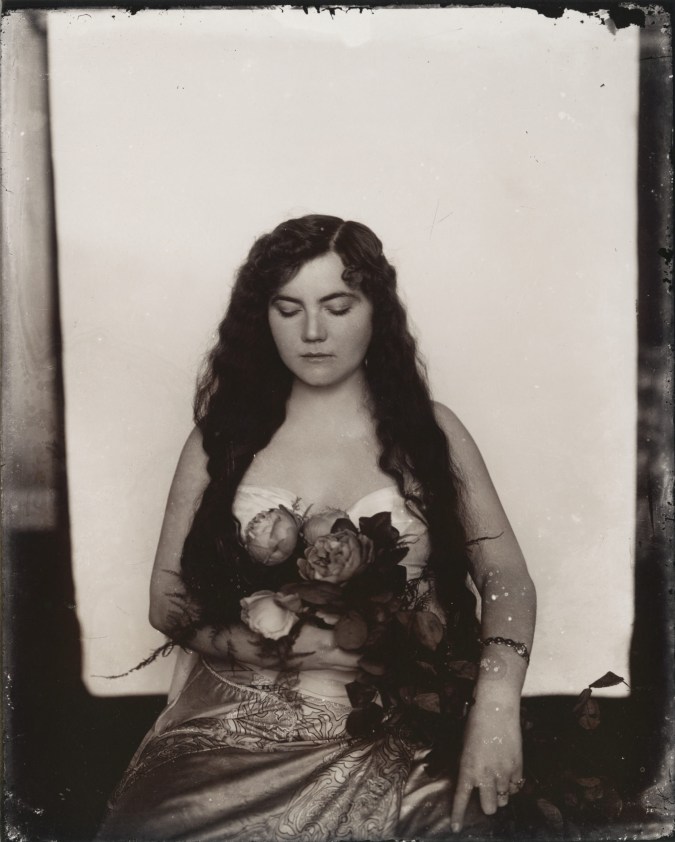 Black and white photograph of a woman holding flowers in front of a white backdrop
