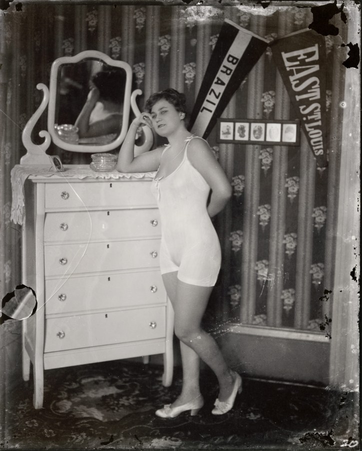 Black and white photograph of a woman in a negligee, leaning with her arm resting on a dresser