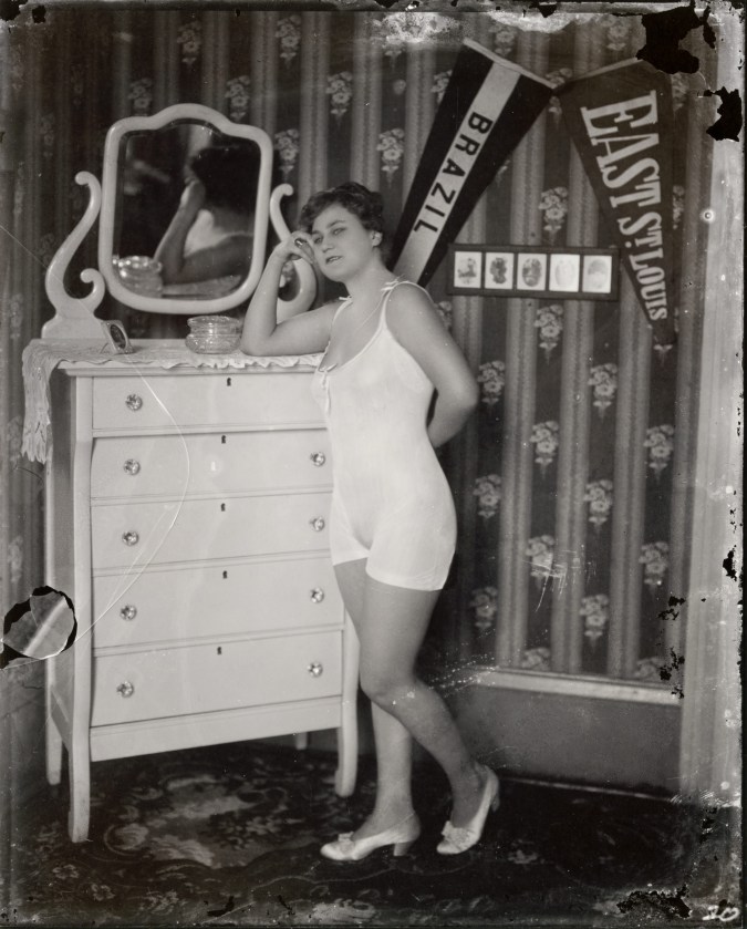 Black and white photograph of a woman in a negligee, leaning with her arm resting on a dresser