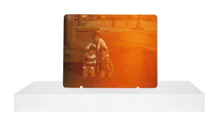 Photorealistic painting of a man kneeling on a suburban lawn with his arms around two little boys mounted on a plain white stand