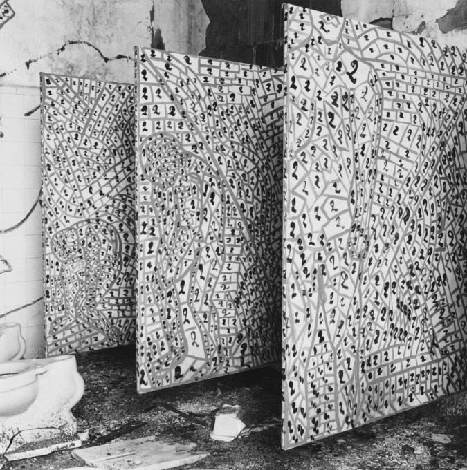 Black-and-white photograph of three painted panels standing in a derelict tiled bathroom