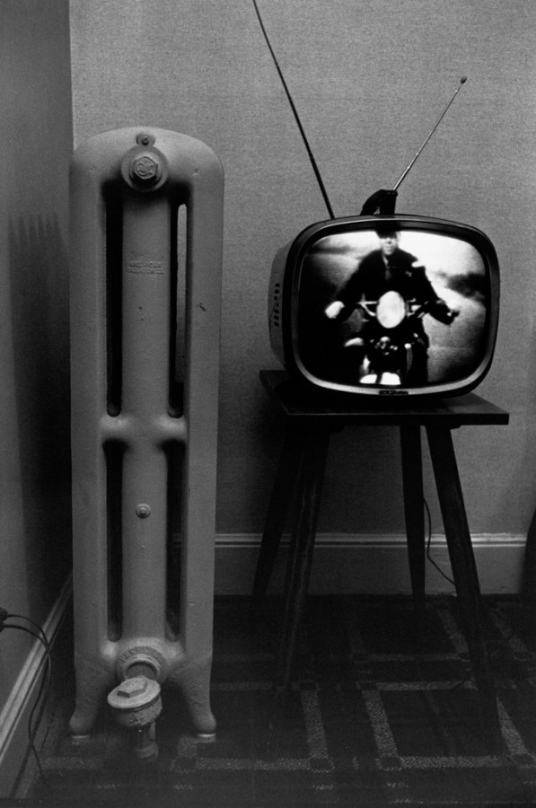 Black-and-white photograph of a television with a motorcyclist on screen and a radiator