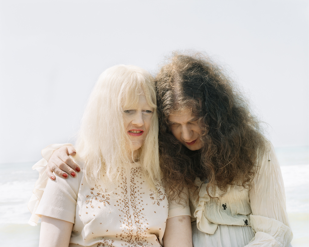 Color photograph of two older women seated side-by-side in front of waves on the beach