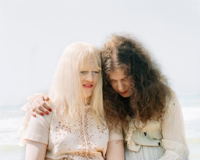 Color photograph of two older women seated side-by-side in front of waves on the beach