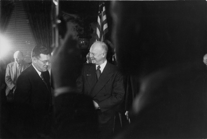Black-and-white photograph of older man in suit through a crowded foreground