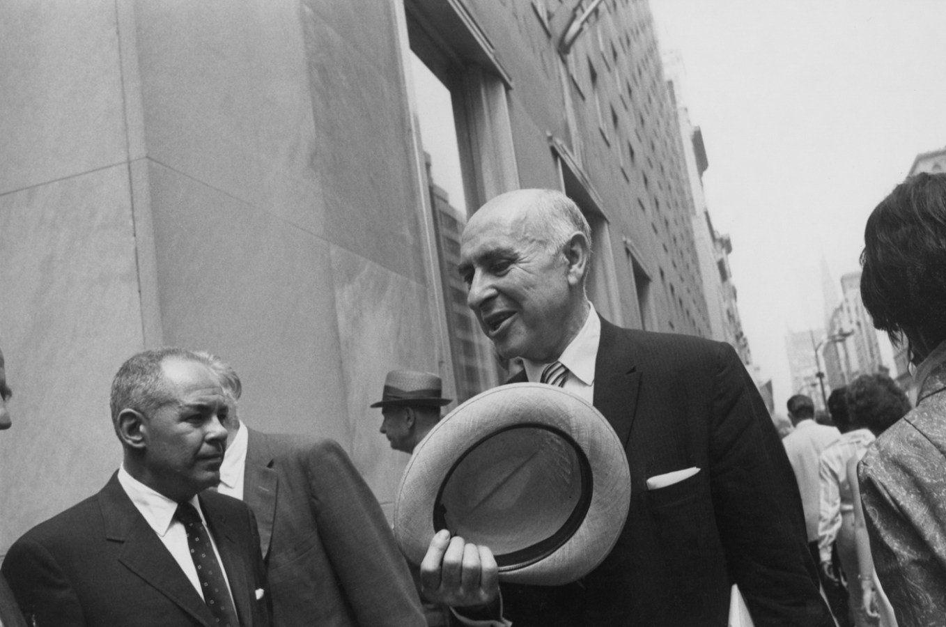 Black-and-white photograph of an older balding man in a suit holding a straw hat