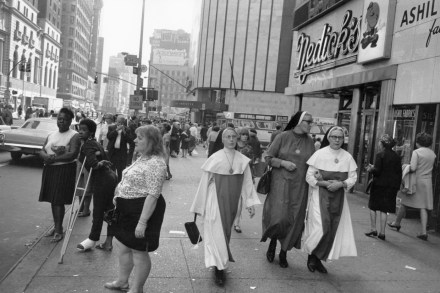 Black and white photograph of bustling city street with three nuns walking in unison