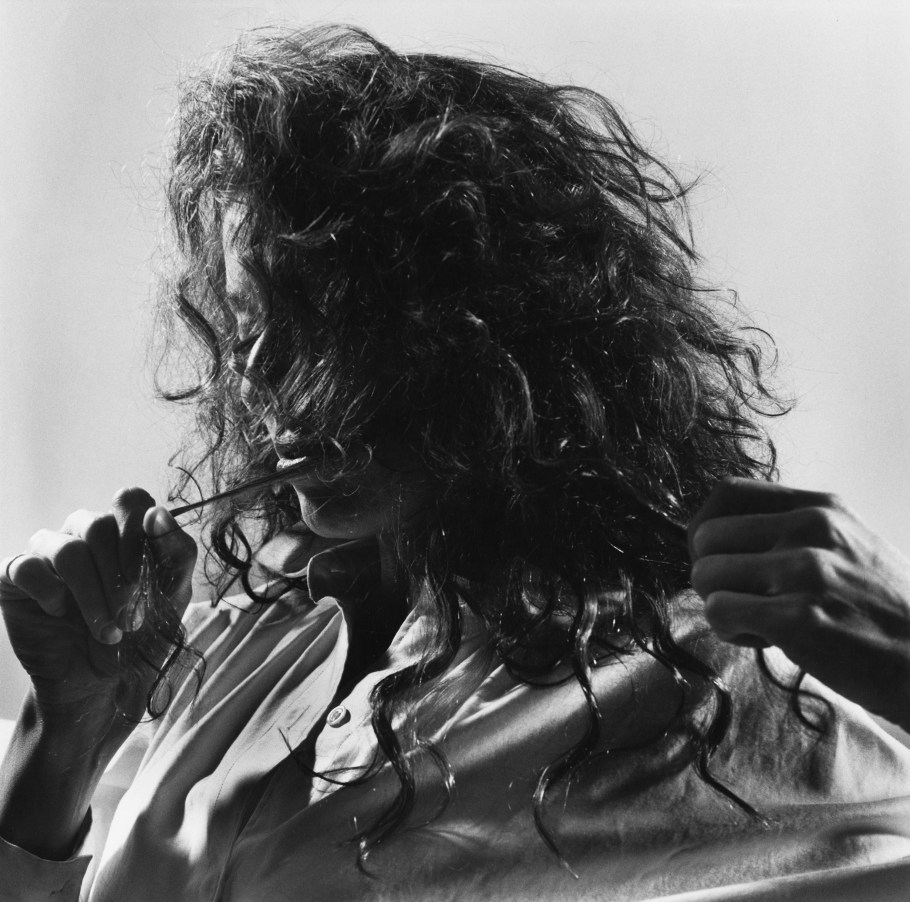 Black and white photograph of a figure from the shoulders up with their hair in their face and hands