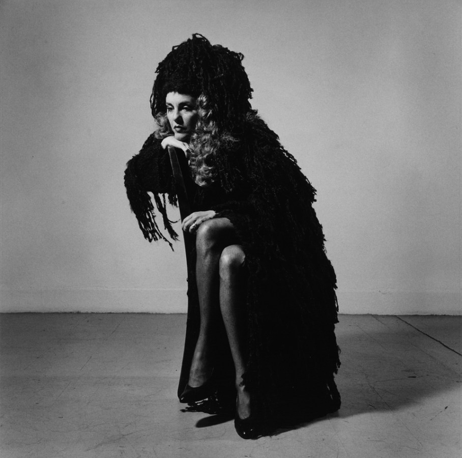 Black-and-white photograph of a woman with long curly hair in a dark wooly shawl seated sideways with her chin on her hand