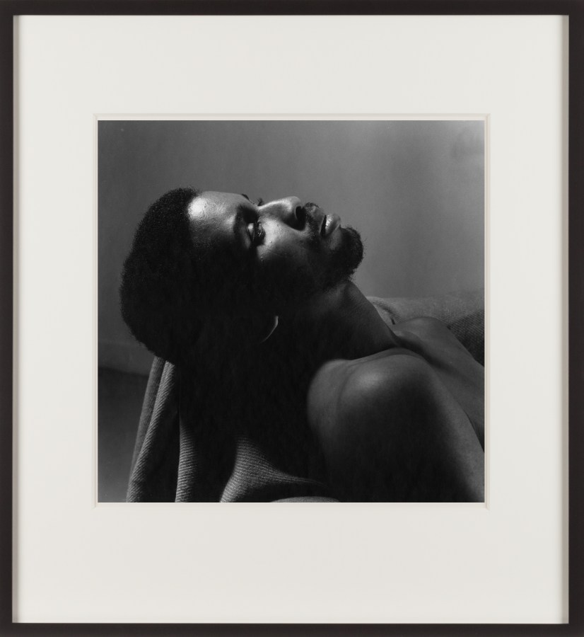 Black and white photograph of a figure resting from the chest up, looking upwards framed in black