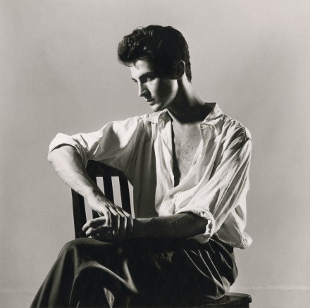 Black and white photo of a person sitting casually in a chair looking away from the camera
