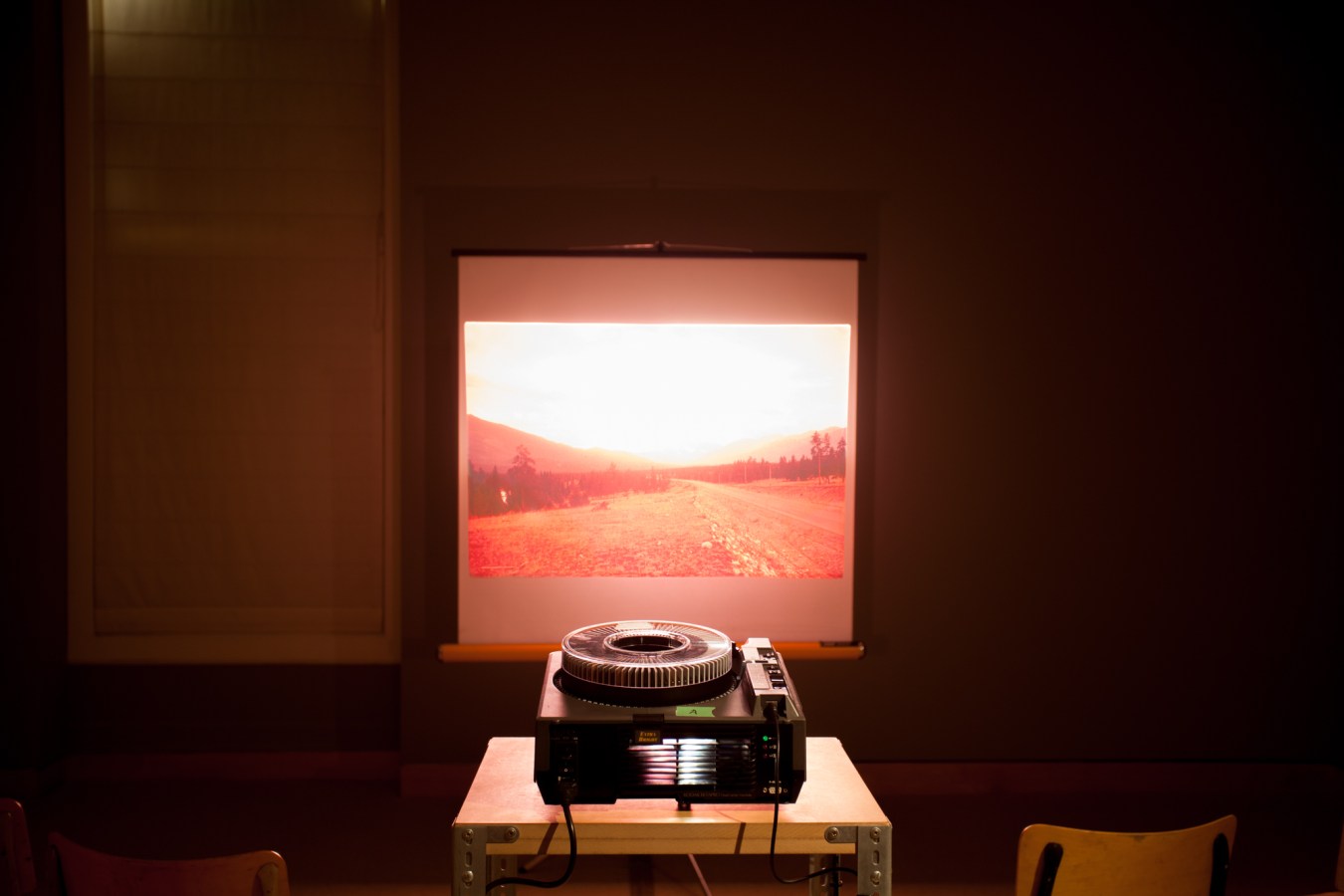 A slide projector projects an image of a landscape onto a screen in a darkened room