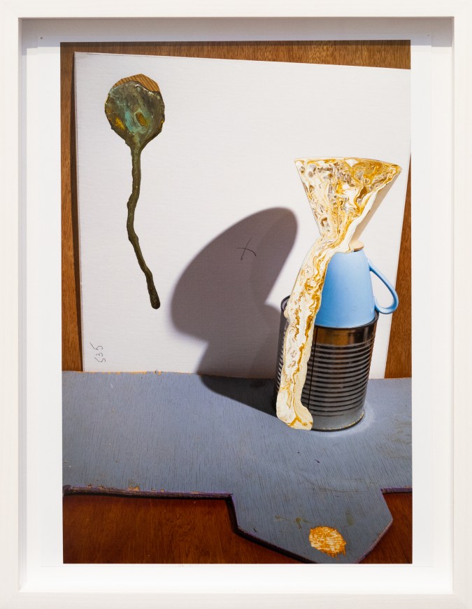 Color photograph with abstract paint splotches framed in white depicting a still life of utilitarian objects