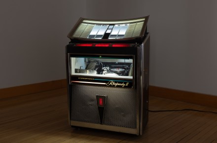 Color image of a vintage jukebox in a dim white walled gallery
