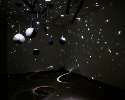 A dark room with lights refracting off hanging mirrored balls creating a star-like reflections on the walls