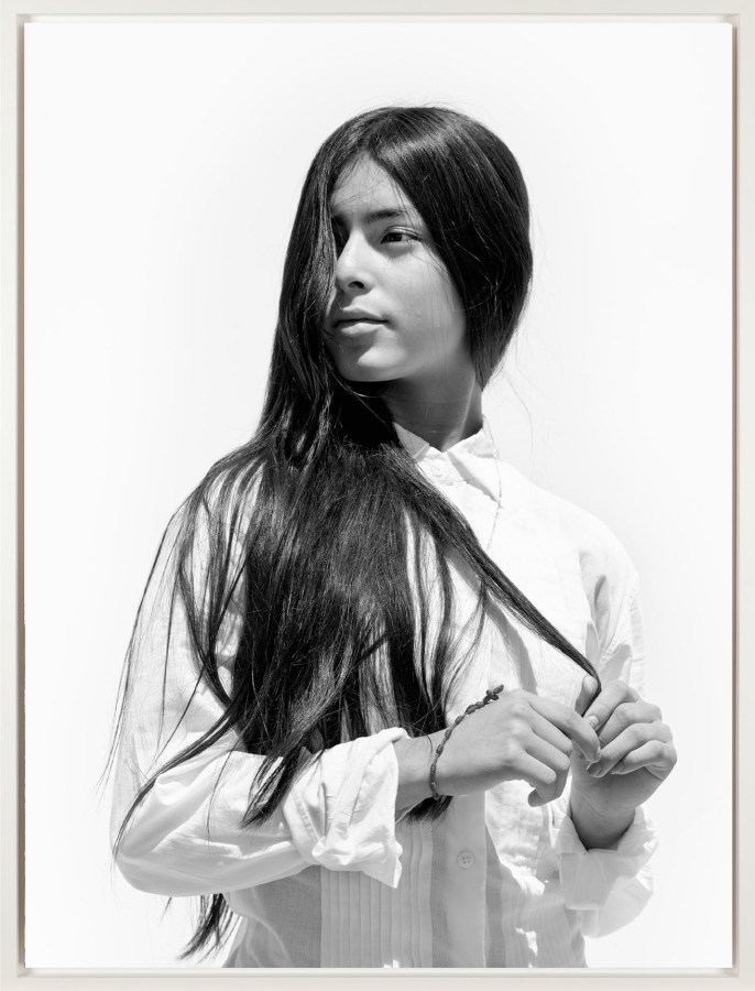 Black and white photograph in white frame of girl in white button up with hair in face and hands