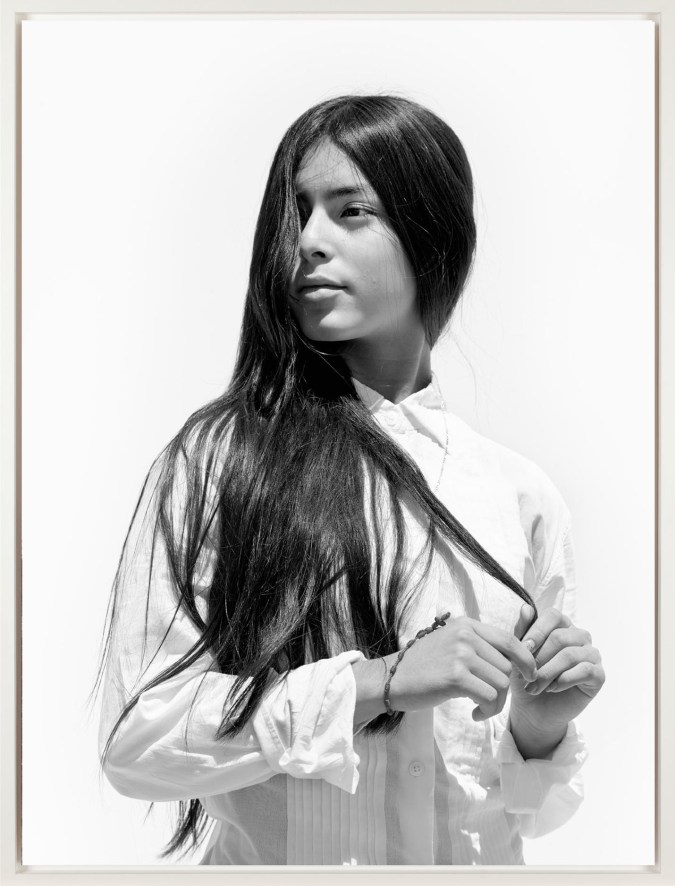 Black and white photograph in white frame of girl in white button up with hair in face and hands