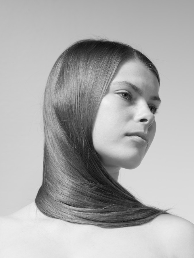 Black and white photograph of a figure from the shoulders up with hair wrapped around their neck