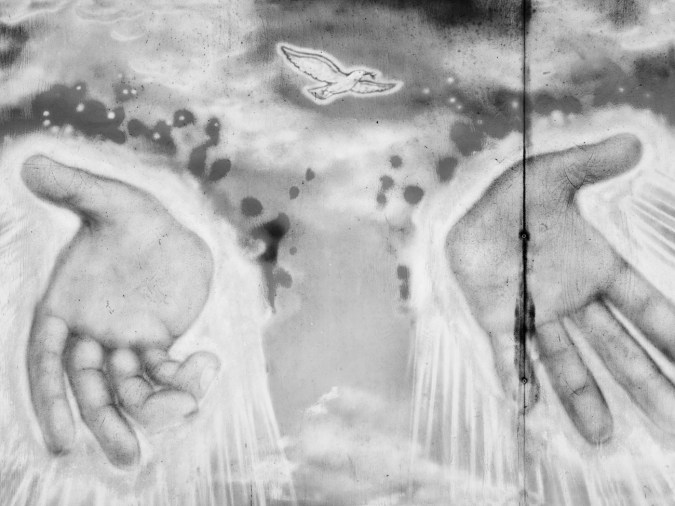 Black-and-white photograph of a wall painting of a flying dove and two hands emanating rays of light