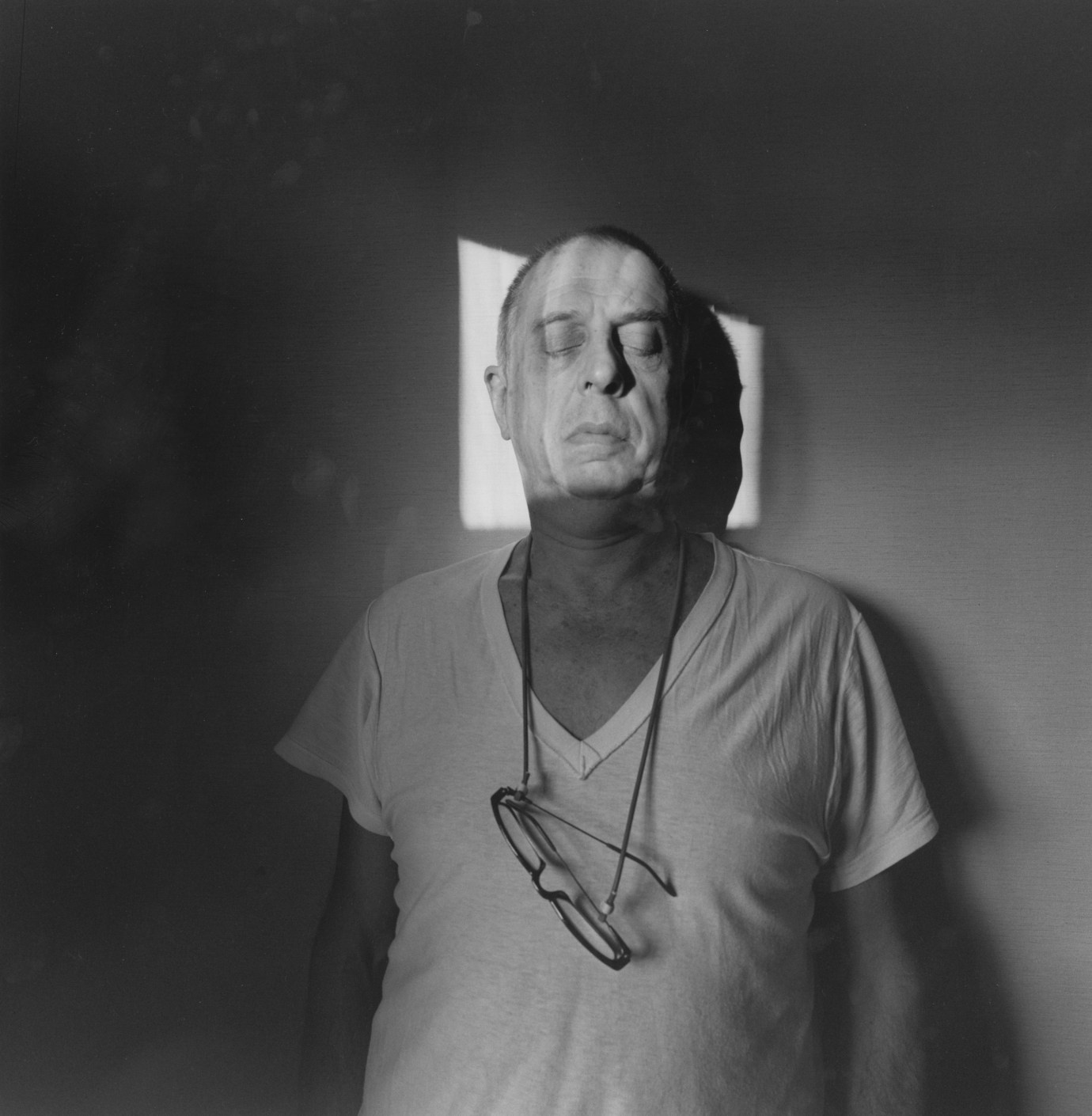 A black and white self portrait of Lee, up against a wall with his eyes closed, his head in a square of light.