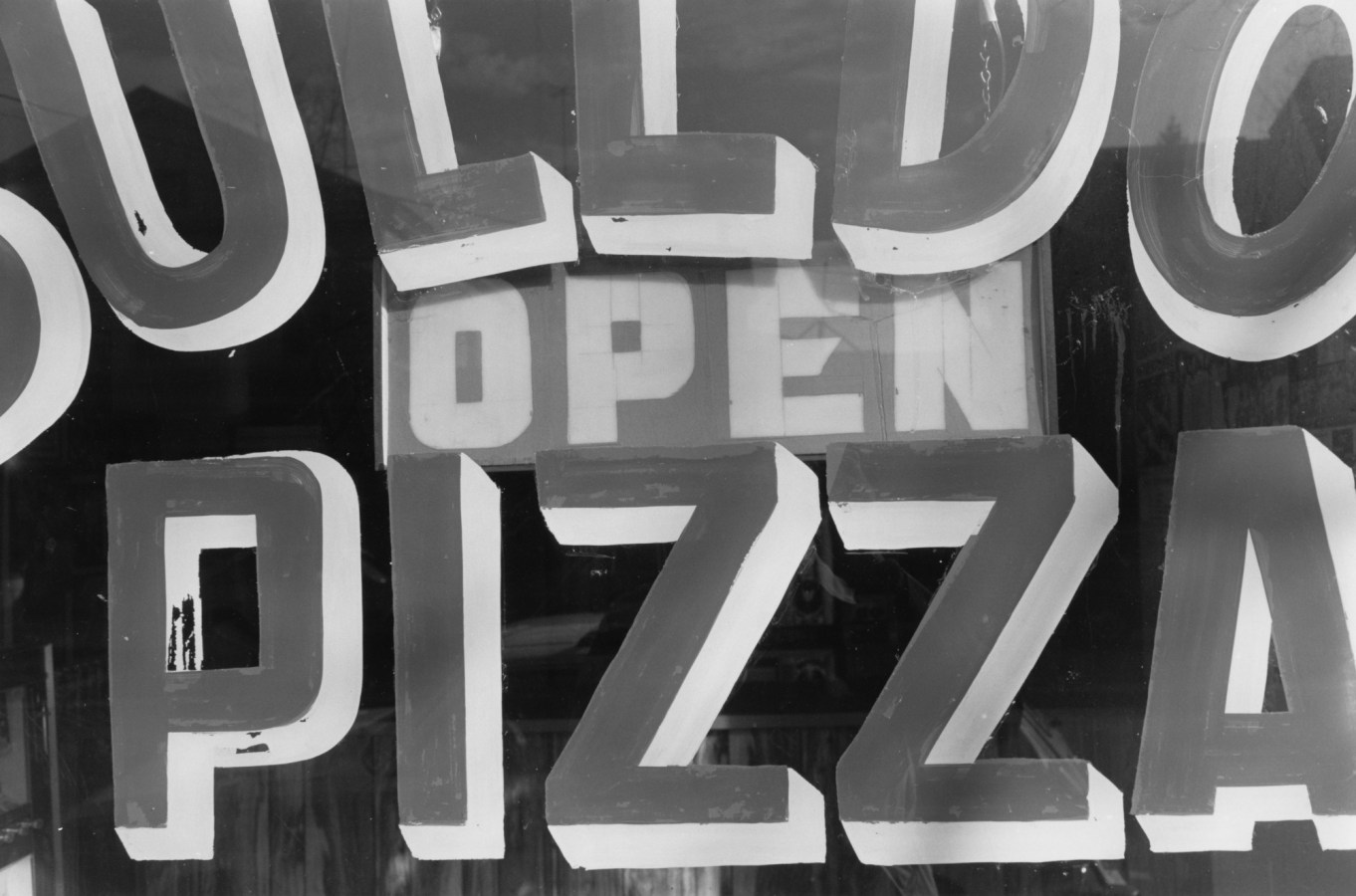 Black-and-white photograph showing detail of a sign with the text open pizza